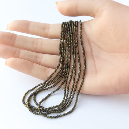 A person holds delicate strands of Cat's Eye beads, showcasing their faceted rondelle design.
