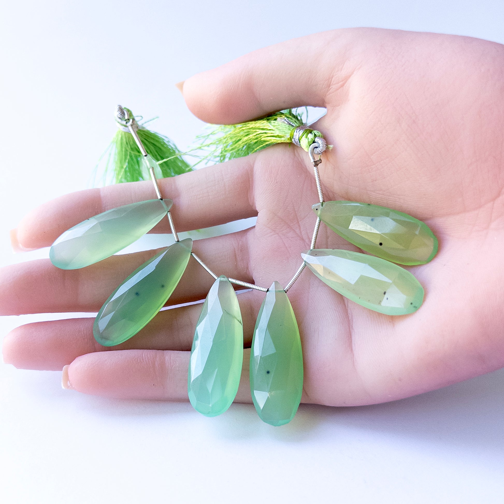 A person holds delicate strands of Chalcedony beads, showcasing their faceted briolette design.