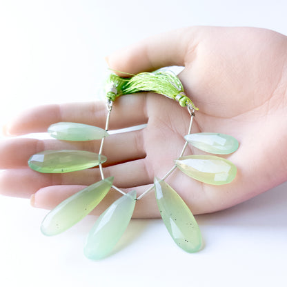 A person holds delicate strands of Chalcedony beads, showcasing their faceted briolette design.