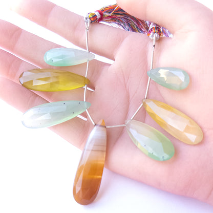 A person holds Chalcedony briolette pieces, showcasing their faceted teardrop design and size variation.
