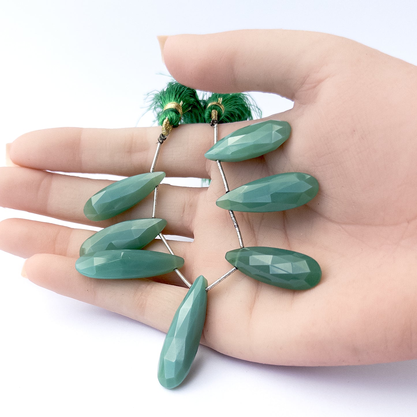 A person holds delicate strands of Chalcedony beads, showcasing their faceted briolette design.