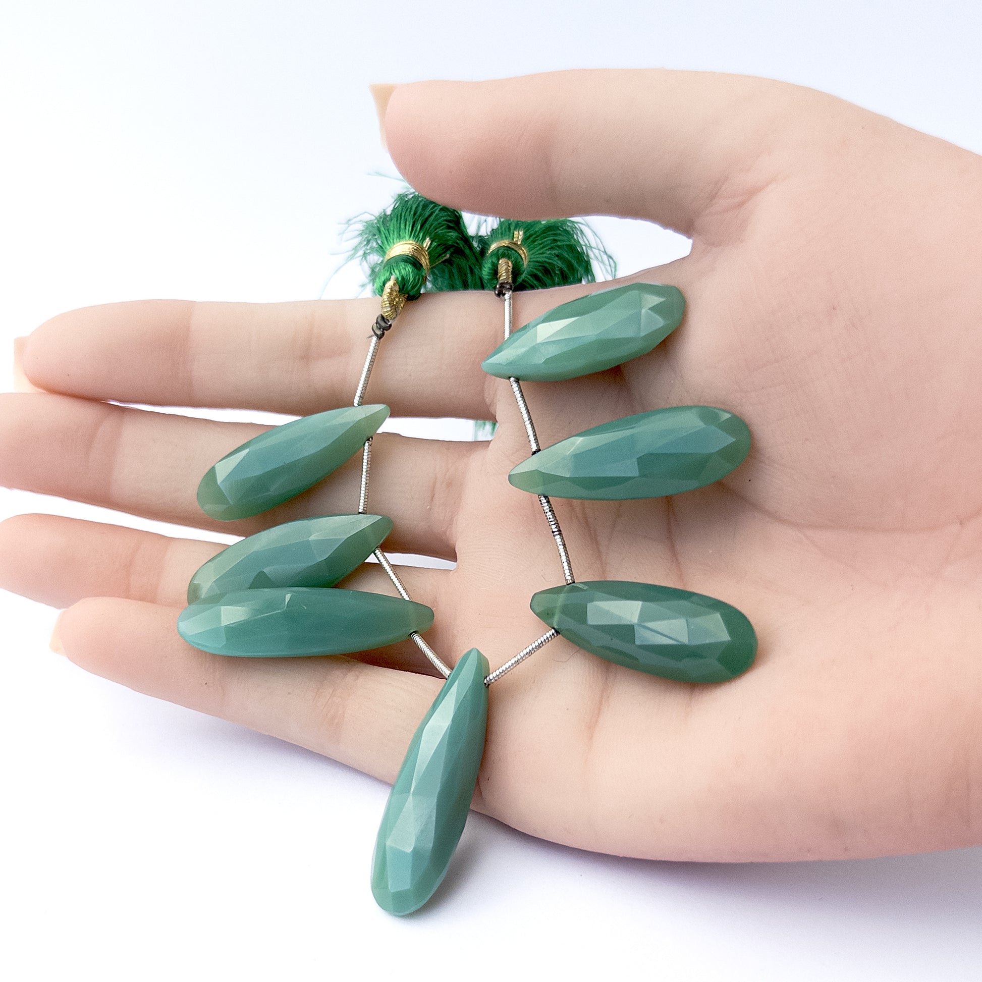 A person holds delicate strands of Chalcedony beads, showcasing their faceted briolette design.