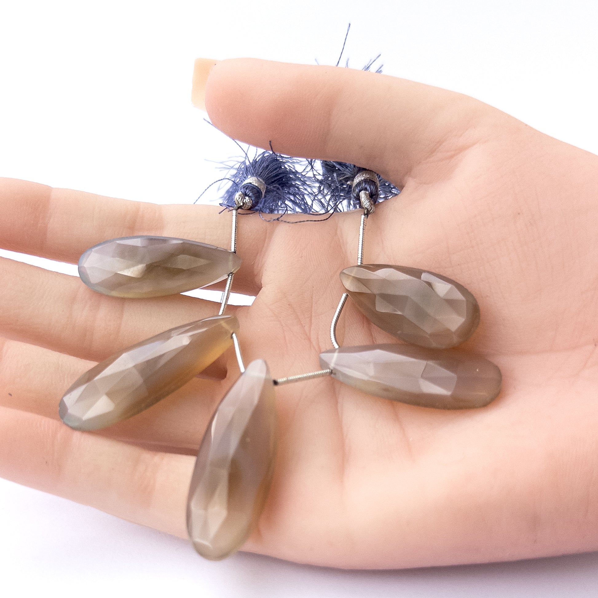 A person holds delicate pieces of Chalcedony beads, showcasing their faceted briolette design.