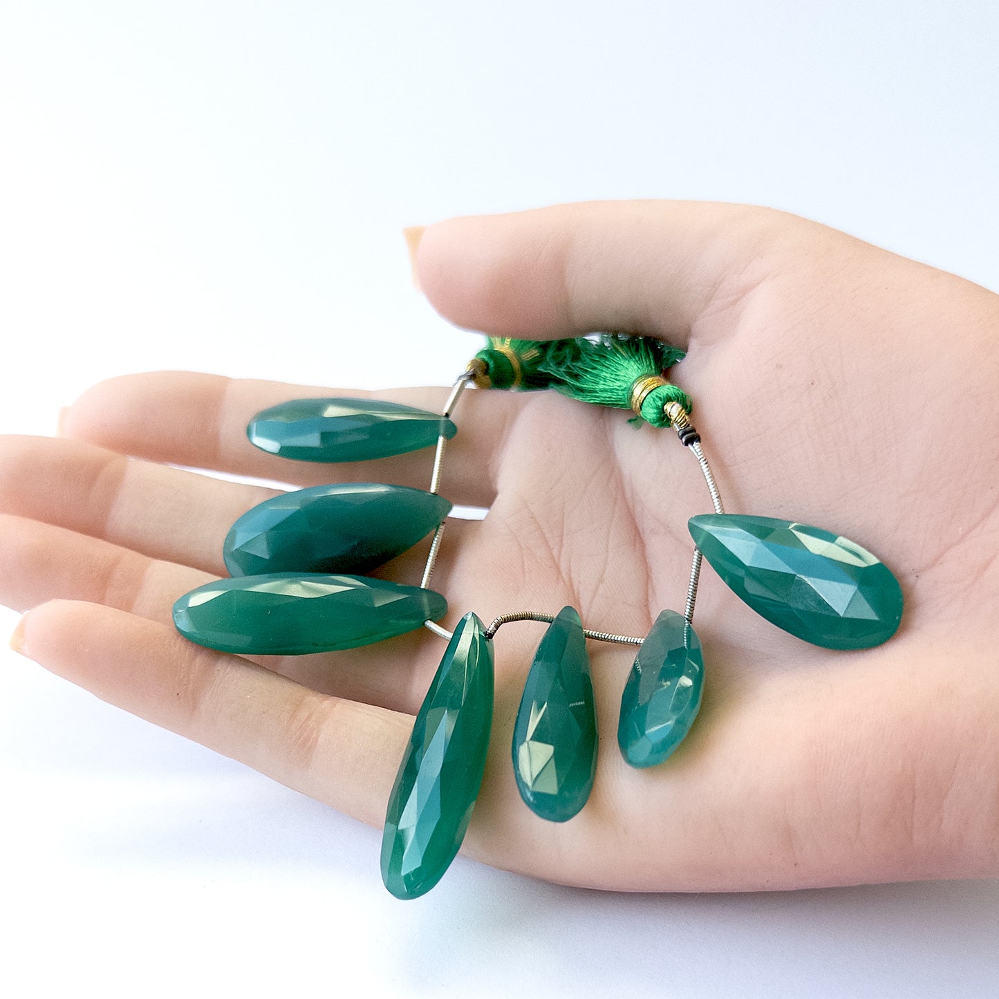 A person holds delicate pieces of Chalcedony beads, showcasing their faceted briolette design.