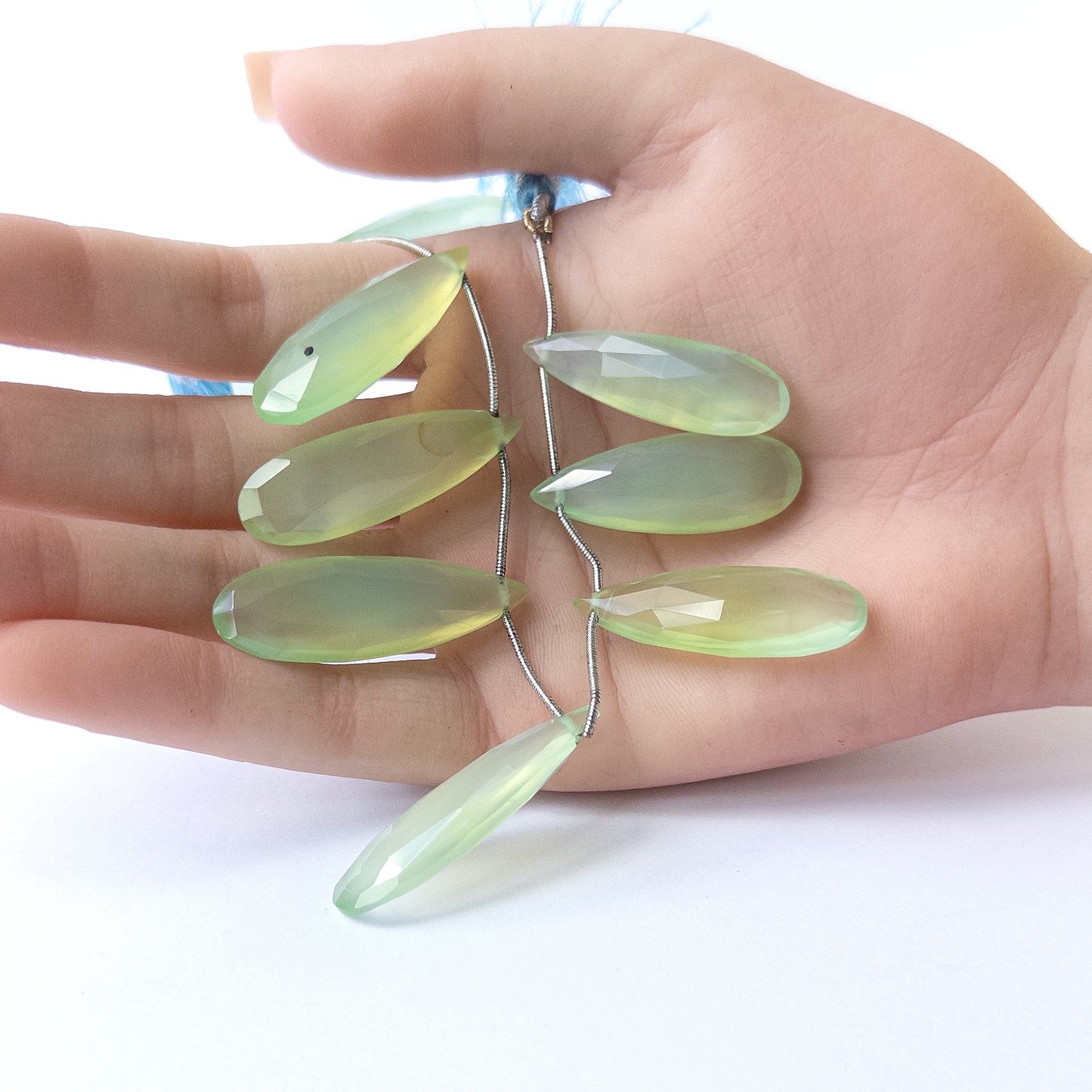 A person holds delicate pieces of Chalcedony beads, showcasing their faceted briolette design.