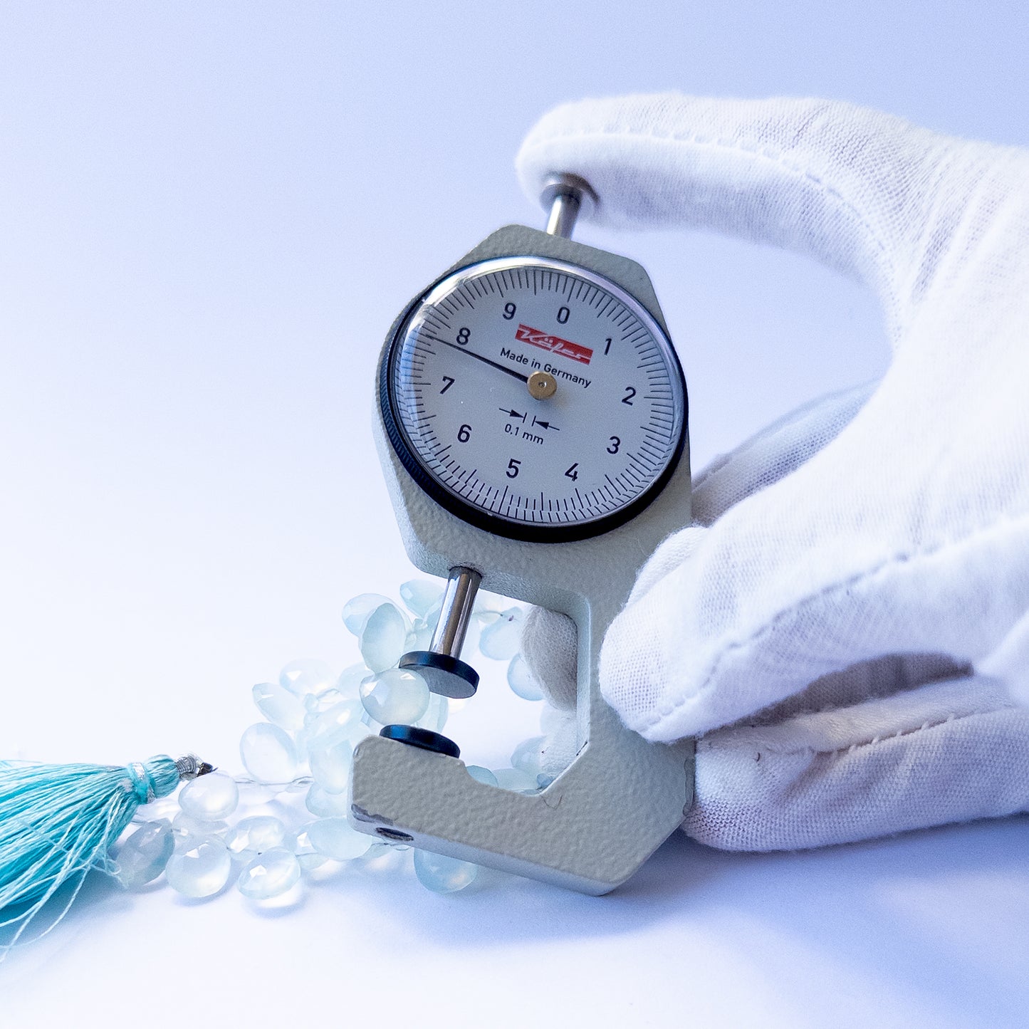 A dial gauge measures the Chalcedony faceted briolette 7–8mm gemstone.