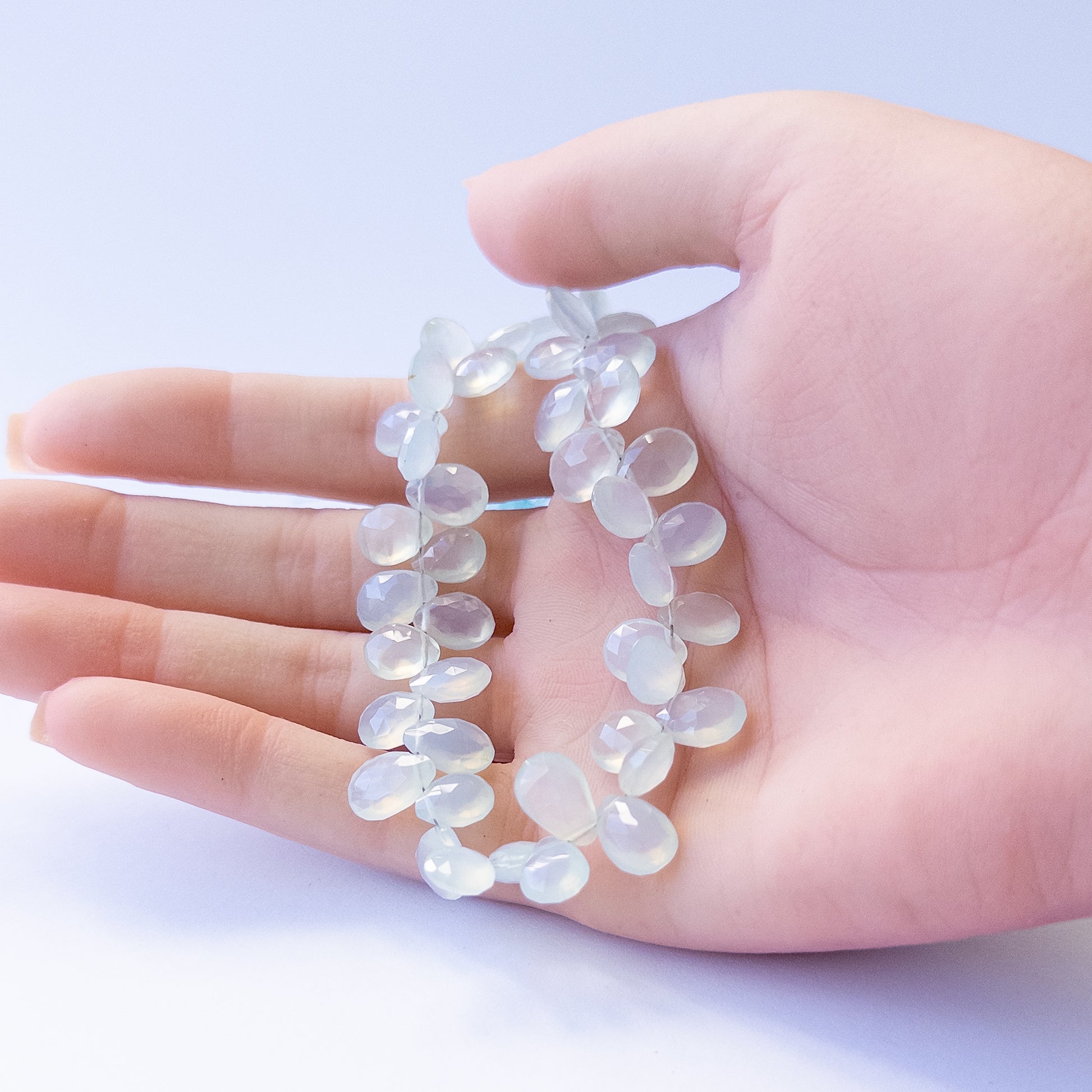 A person holds delicate strands of Chalcedony beads, showcasing their faceted briolette design.