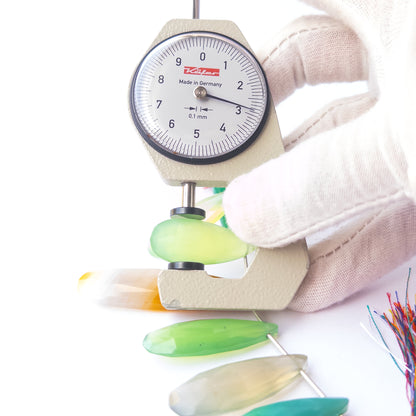 A dial gauge measures the Chalcedony faceted briolette 29–53mm × 9.5–14mm gemstone.