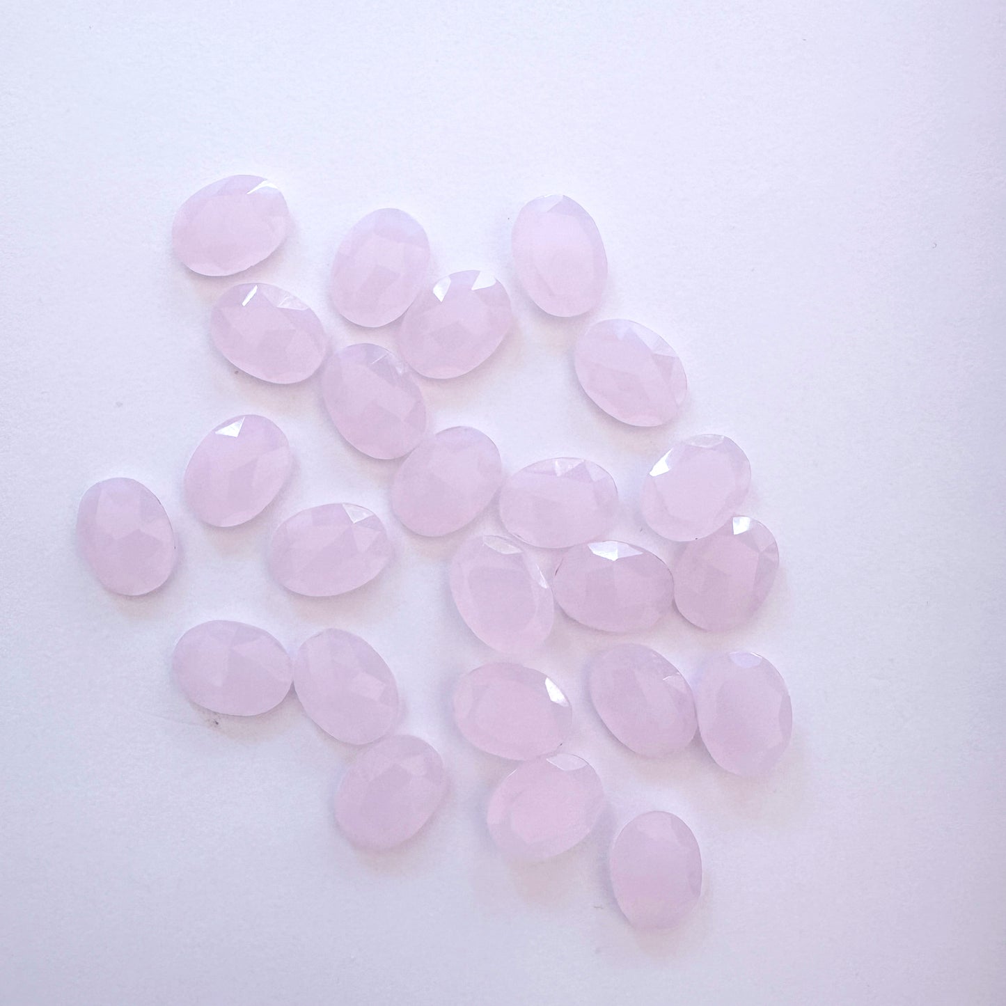 Arrangement of 24 Chalcedony ovals with polished facets and soft colour variation.