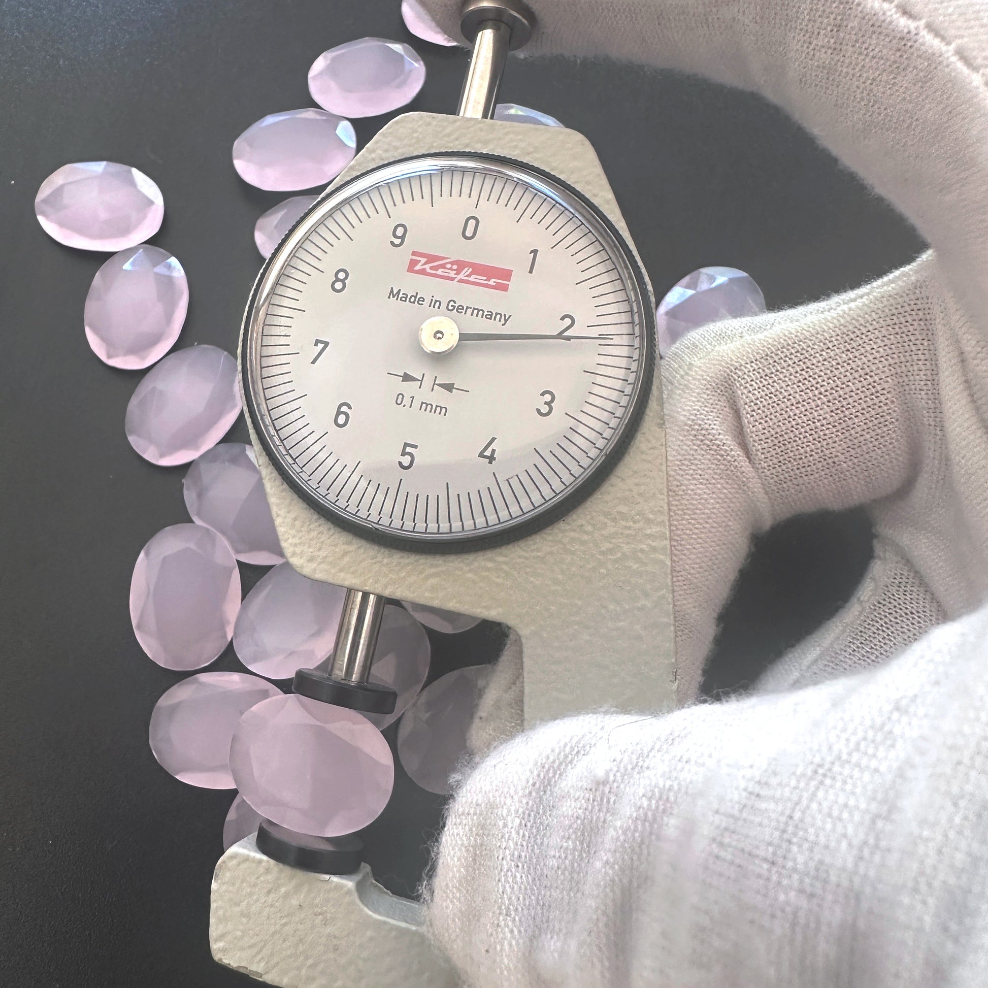A dial gauge measures the Chalcedony faceted oval gemstone's length .