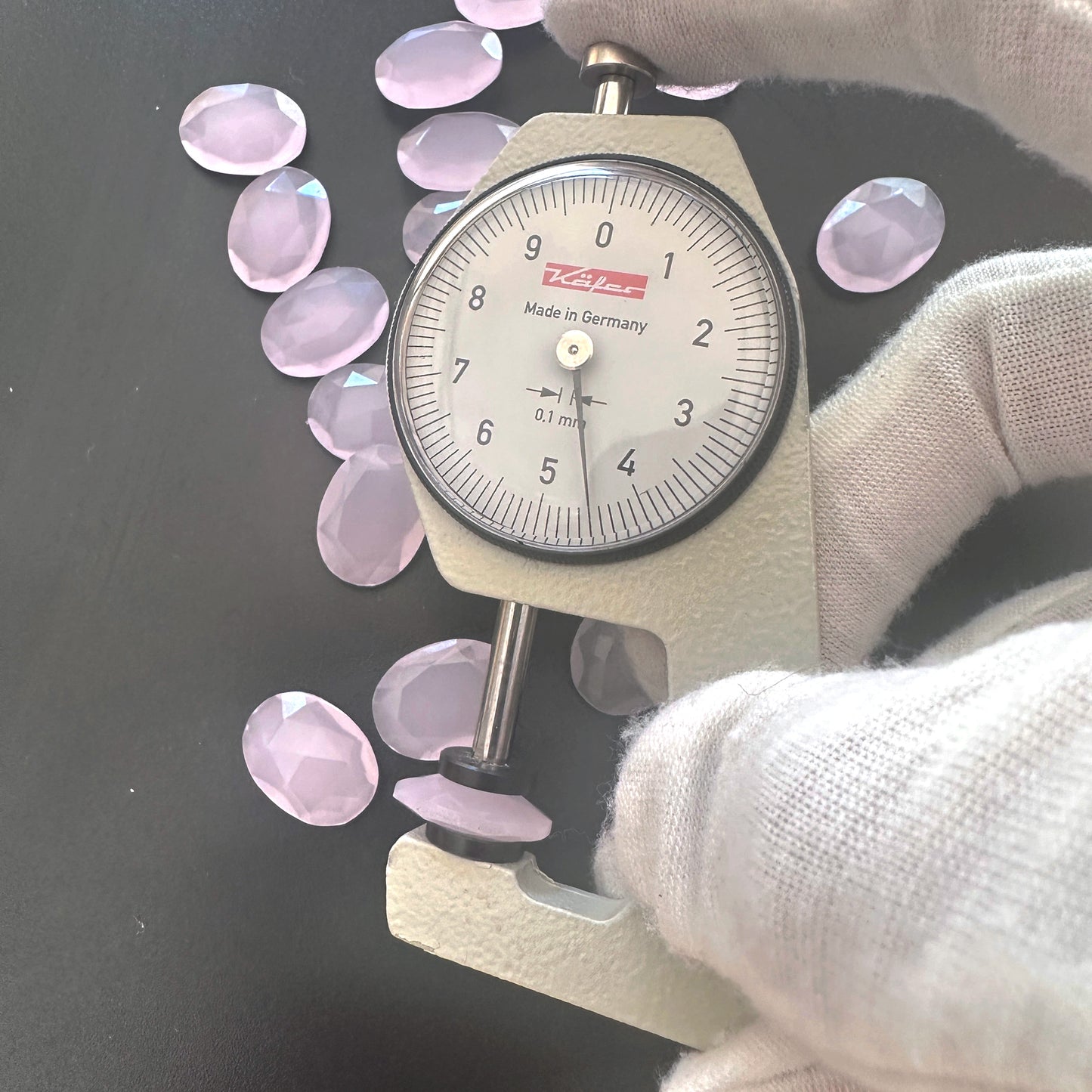 A dial gauge measures the Chalcedony faceted oval gemstone's thickness .