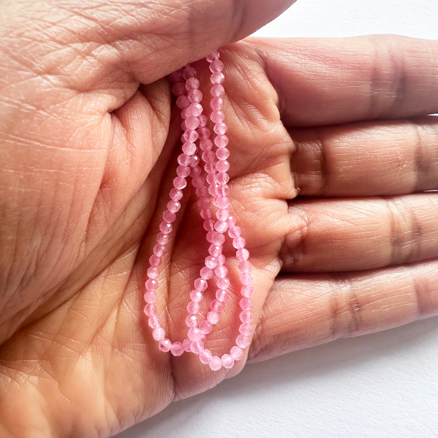 A person holds delicate strands of Chalcedony beads, showcasing their smooth design.