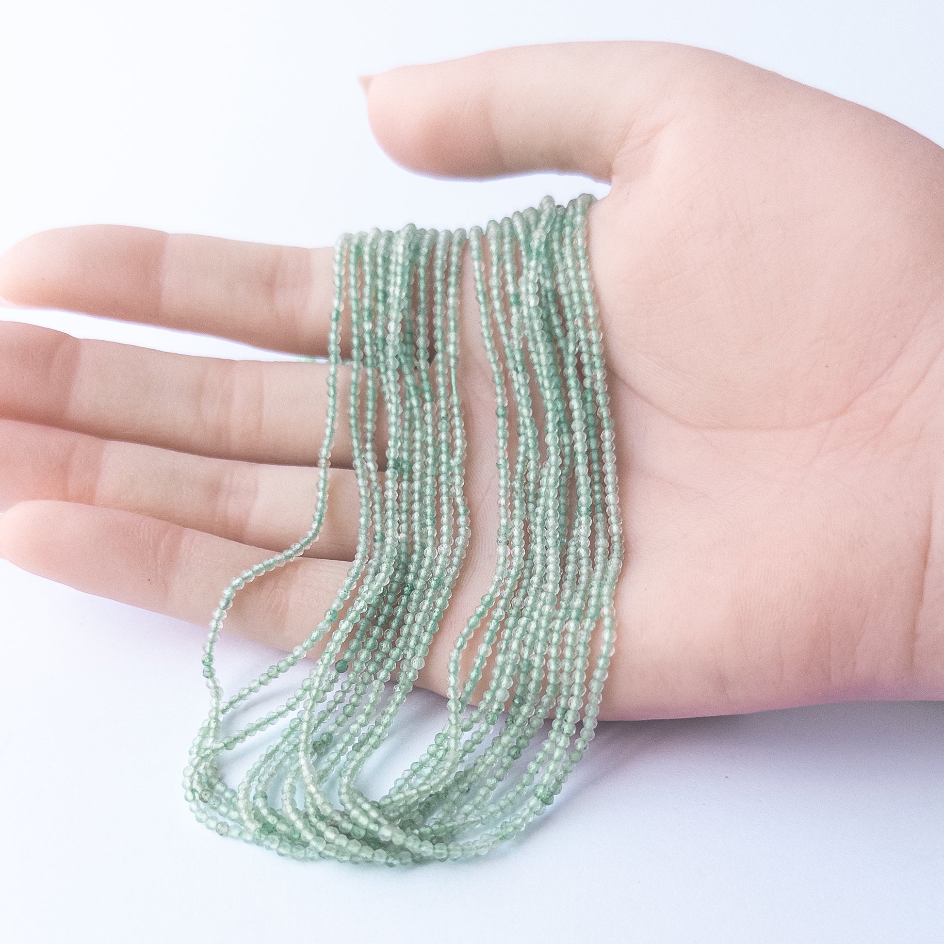 A person holds delicate strands of Chalcedony beads, showcasing their faceted rondelle design.