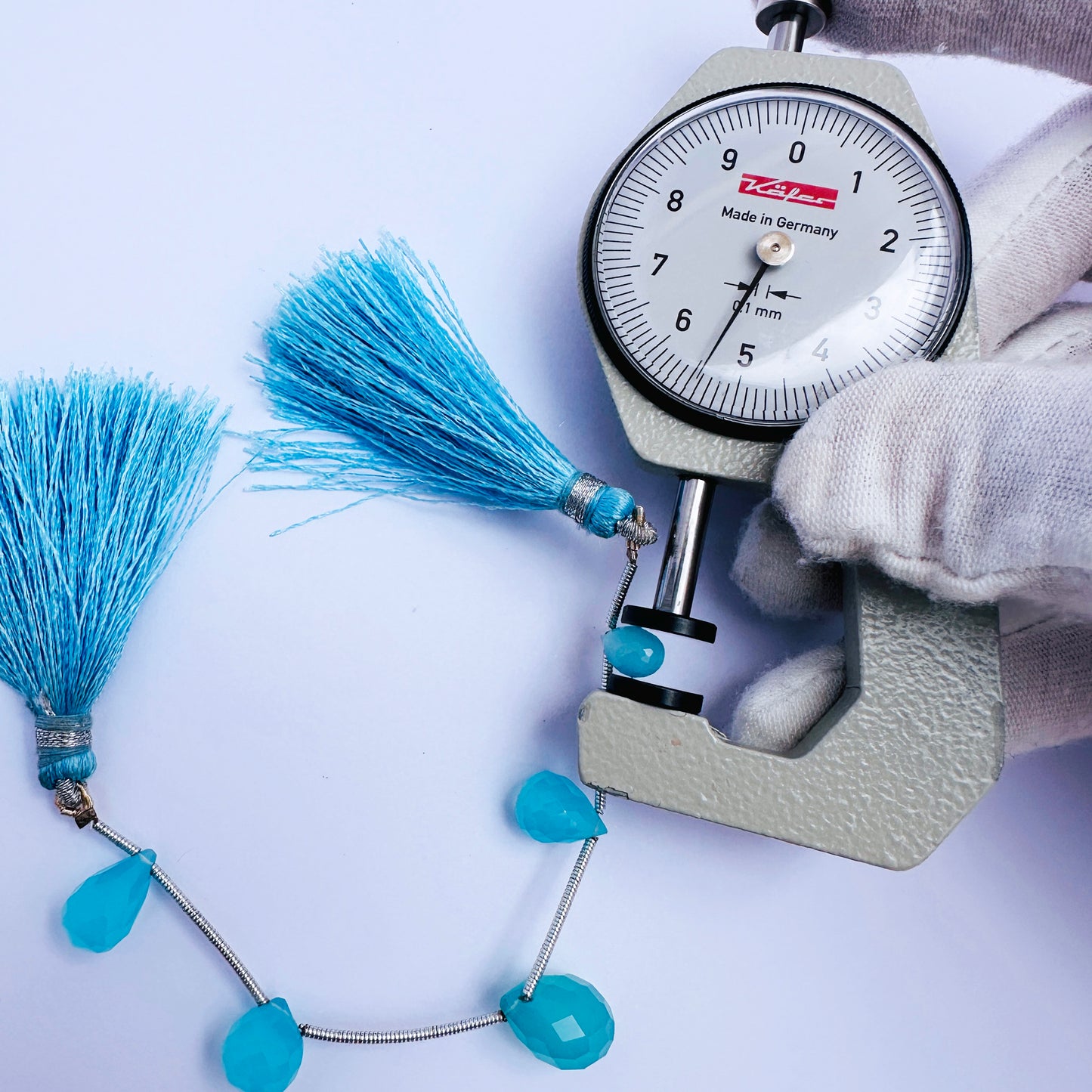 A dial gauge measures the Chalcedony faceted teardrop gemstone.
