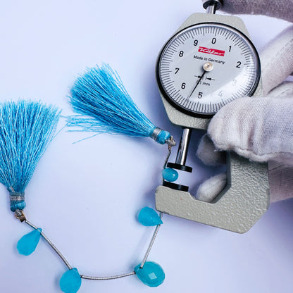 A dial gauge measures the Chalcedony faceted teardrop gemstone.
