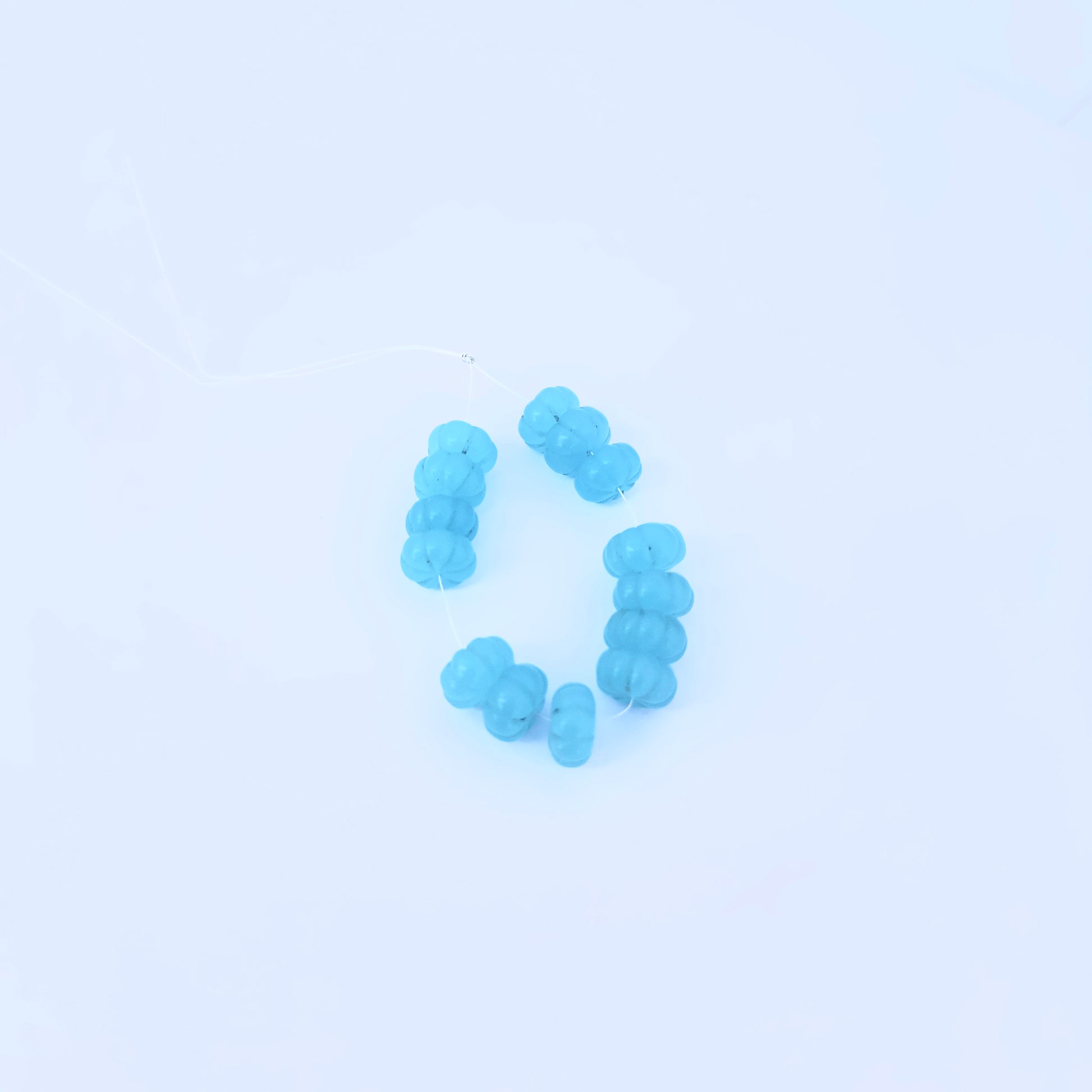 Chalcedony melon cut beads in translucent blue arranged on a white surface for jewellery making.