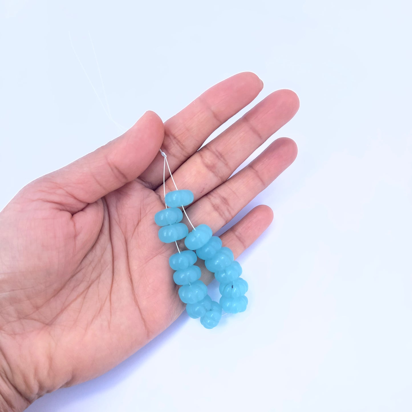 A person holds delicate strands of Chalcedony beads, showcasing their smooth design.