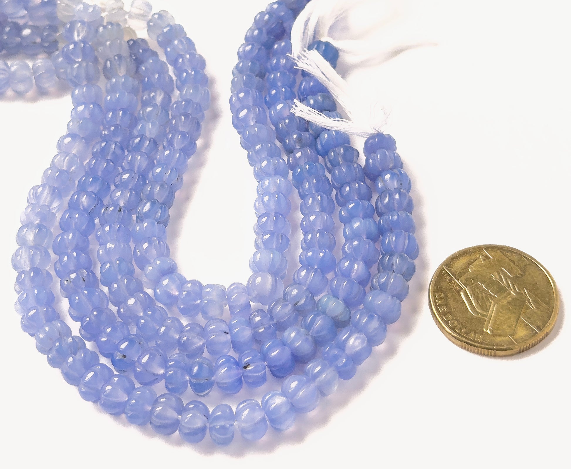 A coin is placed near Chalcedony pumpkin‑cut beads to show the 7.5–8mm size range.