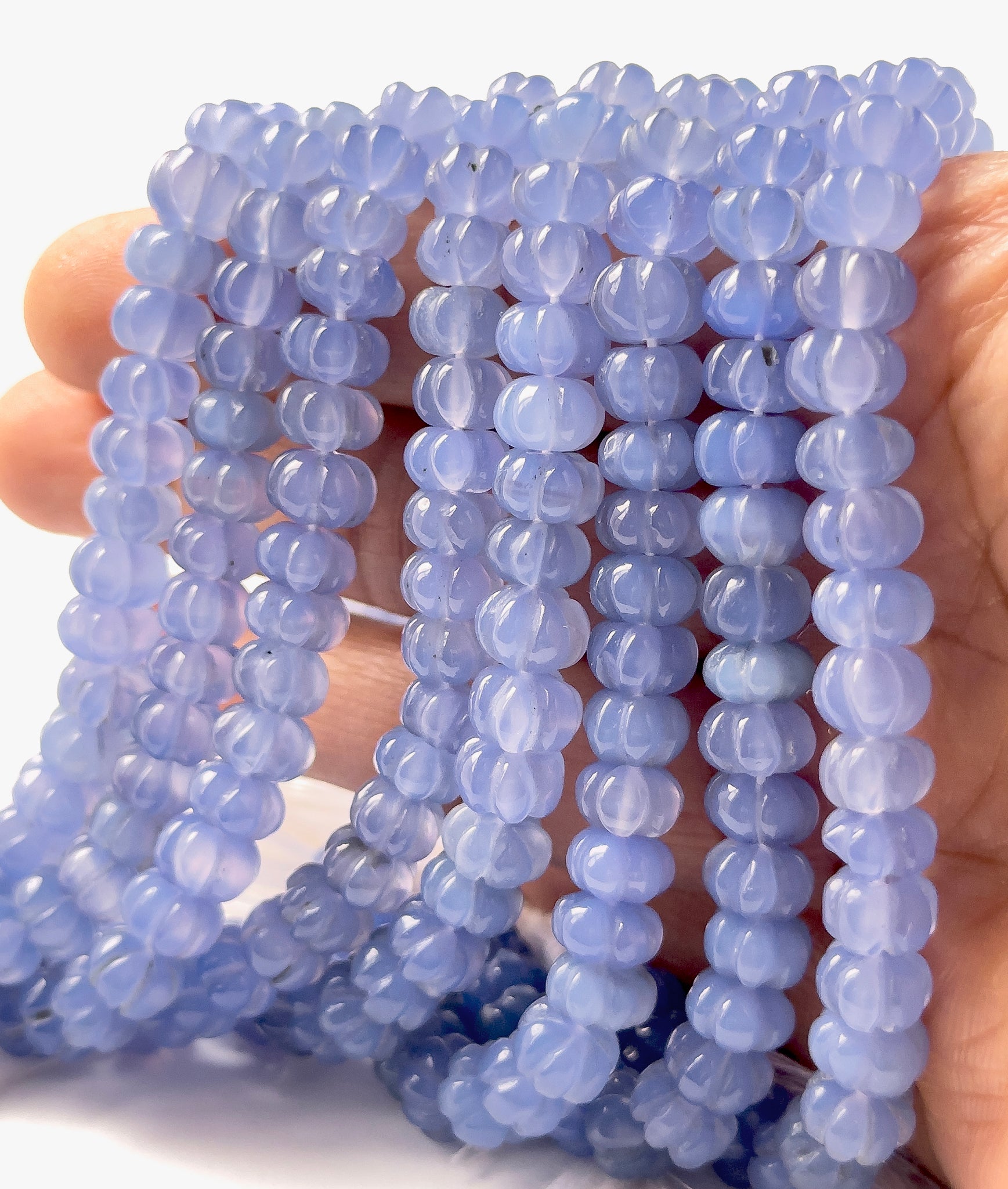 A person holds Chalcedony pumpkin‑cut beads, showing their carved design and soft pastel colour.