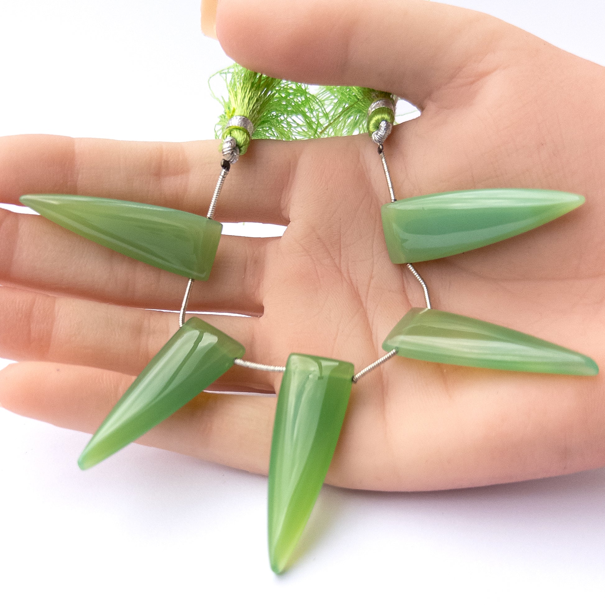 A person holds delicate pieces of Chalcedony beads, showcasing their smooth triangle briolette design.