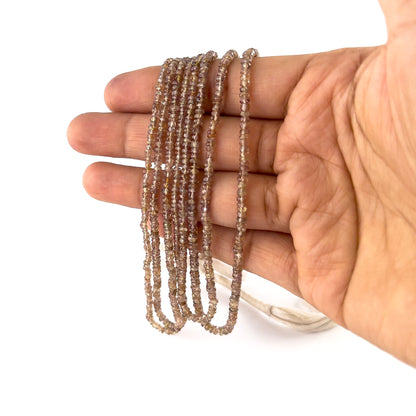 A person holds Change Garnet rondelle beads, showing their faceted design and rich red colour.