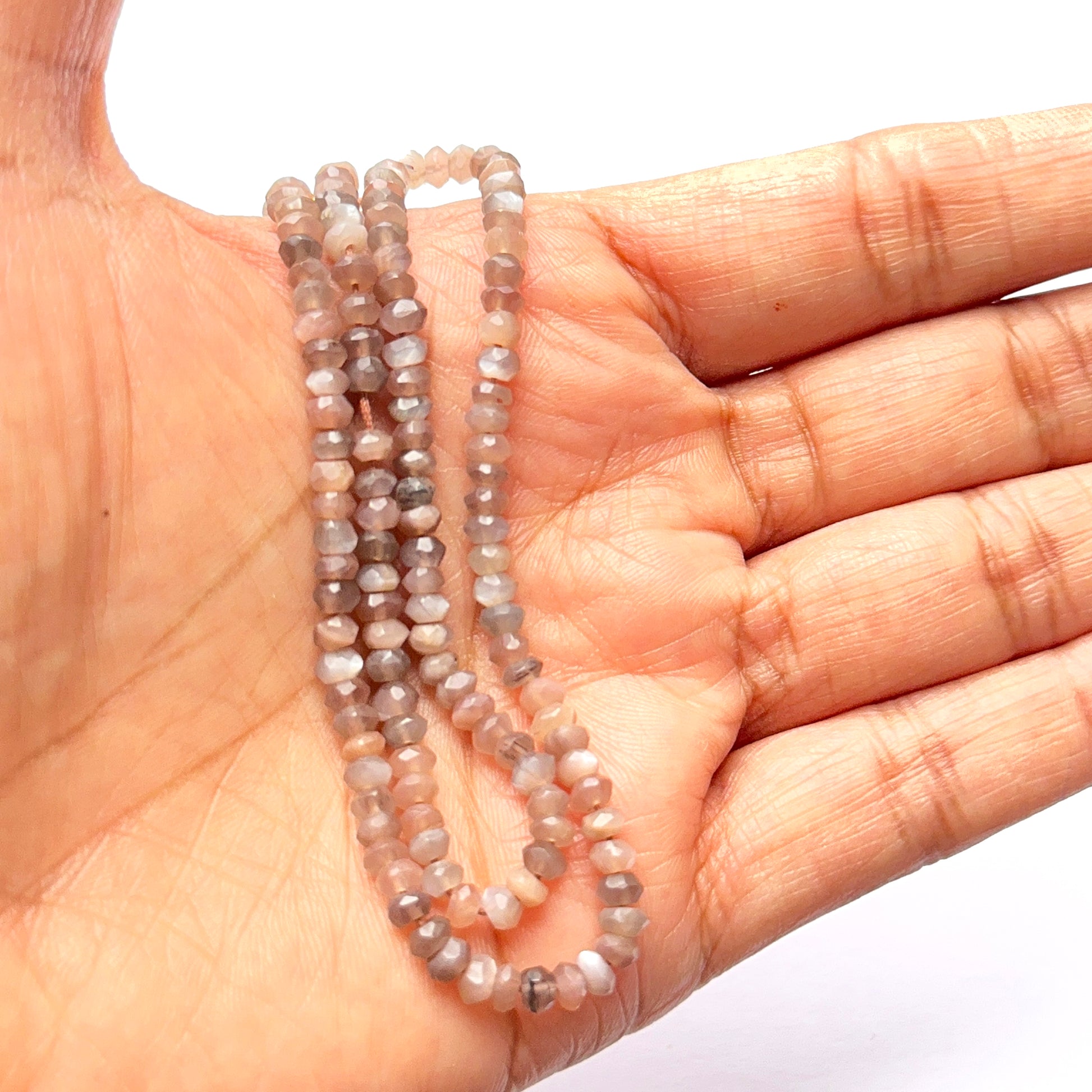 A person holds delicate strands of Chocolate Moonstone beads, showcasing their smooth design.