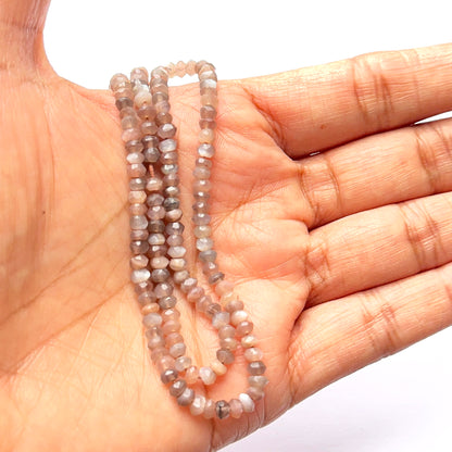 A person holds delicate strands of Chocolate Moonstone beads, showcasing their smooth design.