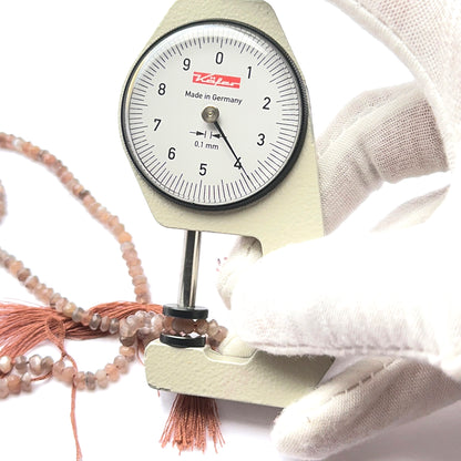 A dial gauge measures the Chocolate Moonstone faceted rondelle 3.8–4mm gemstone.