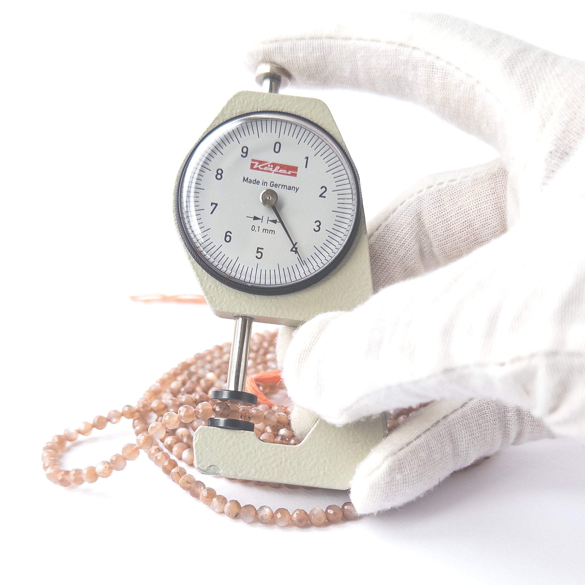 A dial gauge measures the Chocolate Moonstone faceted rondelle 3.8–4mm gemstone.