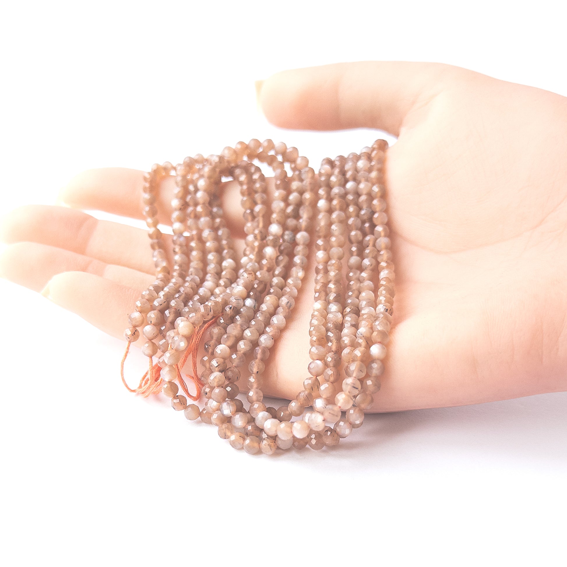 A person holds delicate strands of Chocolate Moonstone faceted rondelle beads, showcasing their cut design.