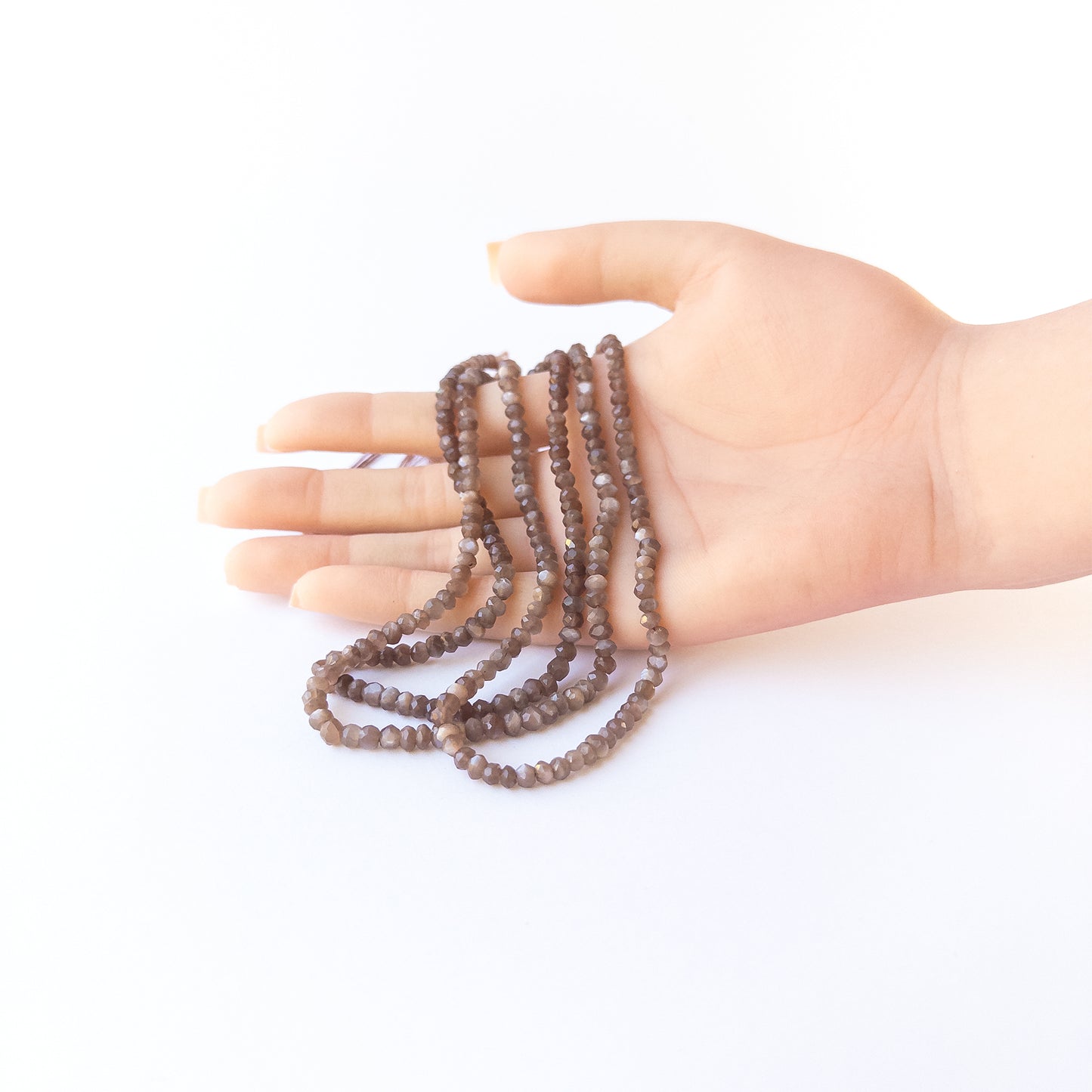 A person holds delicate strands of Chocolate Moonstone beads, showcasing their faceted rondelle design.