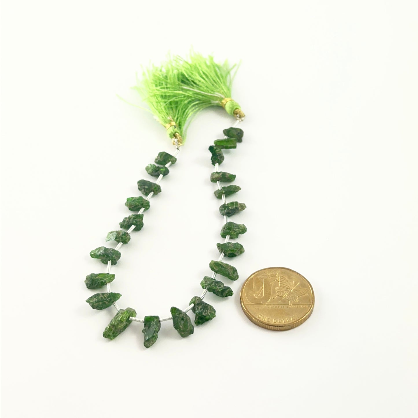 Deep green Chrome Diopside rough stones in 5–6mm sizes for handmade jewellery, set next to a coin for scale.