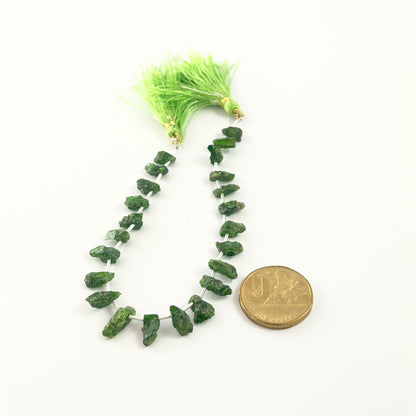 Deep green Chrome Diopside rough stones in 5–6mm sizes for handmade jewellery, set next to a coin for scale.
