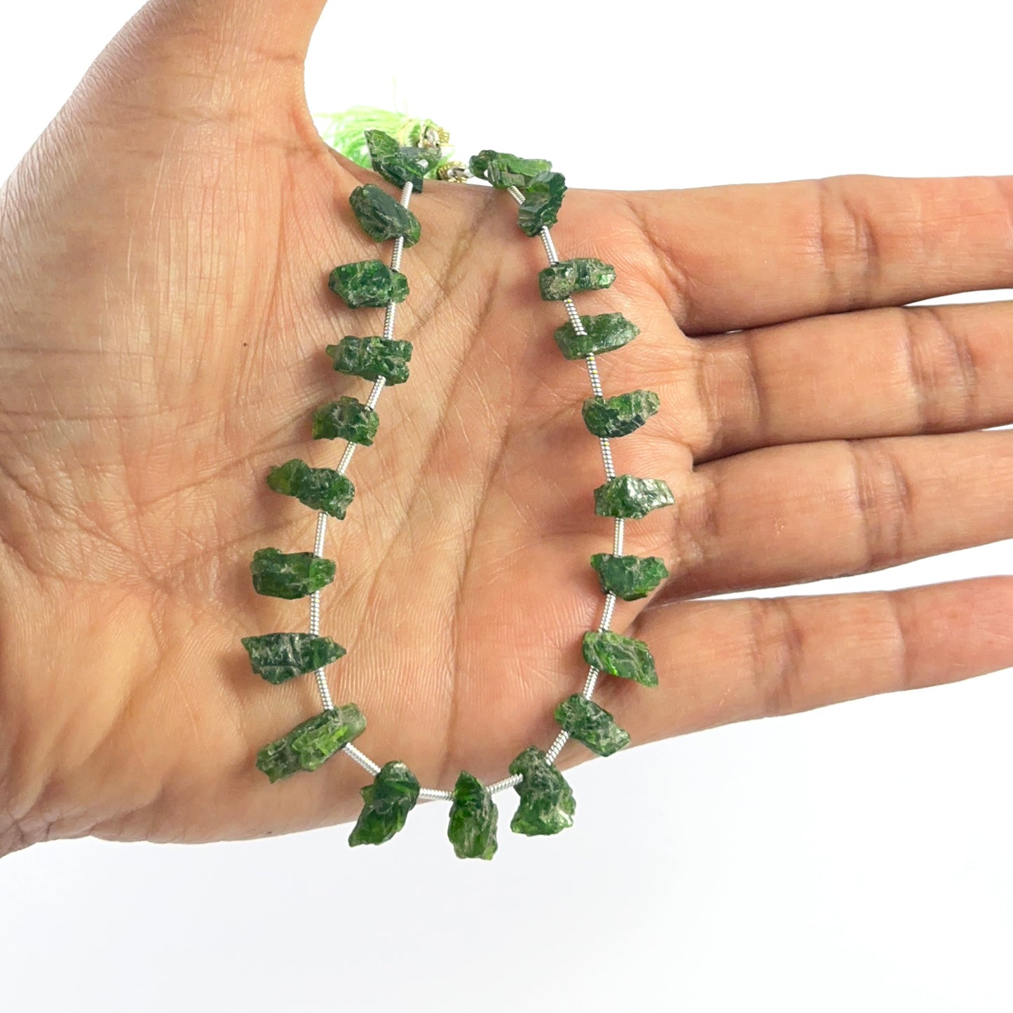 Hand holds high‑quality rough Chrome Diopside beads with natural texture and rich colour