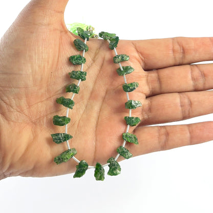 Hand holds high‑quality rough Chrome Diopside beads with natural texture and rich colour