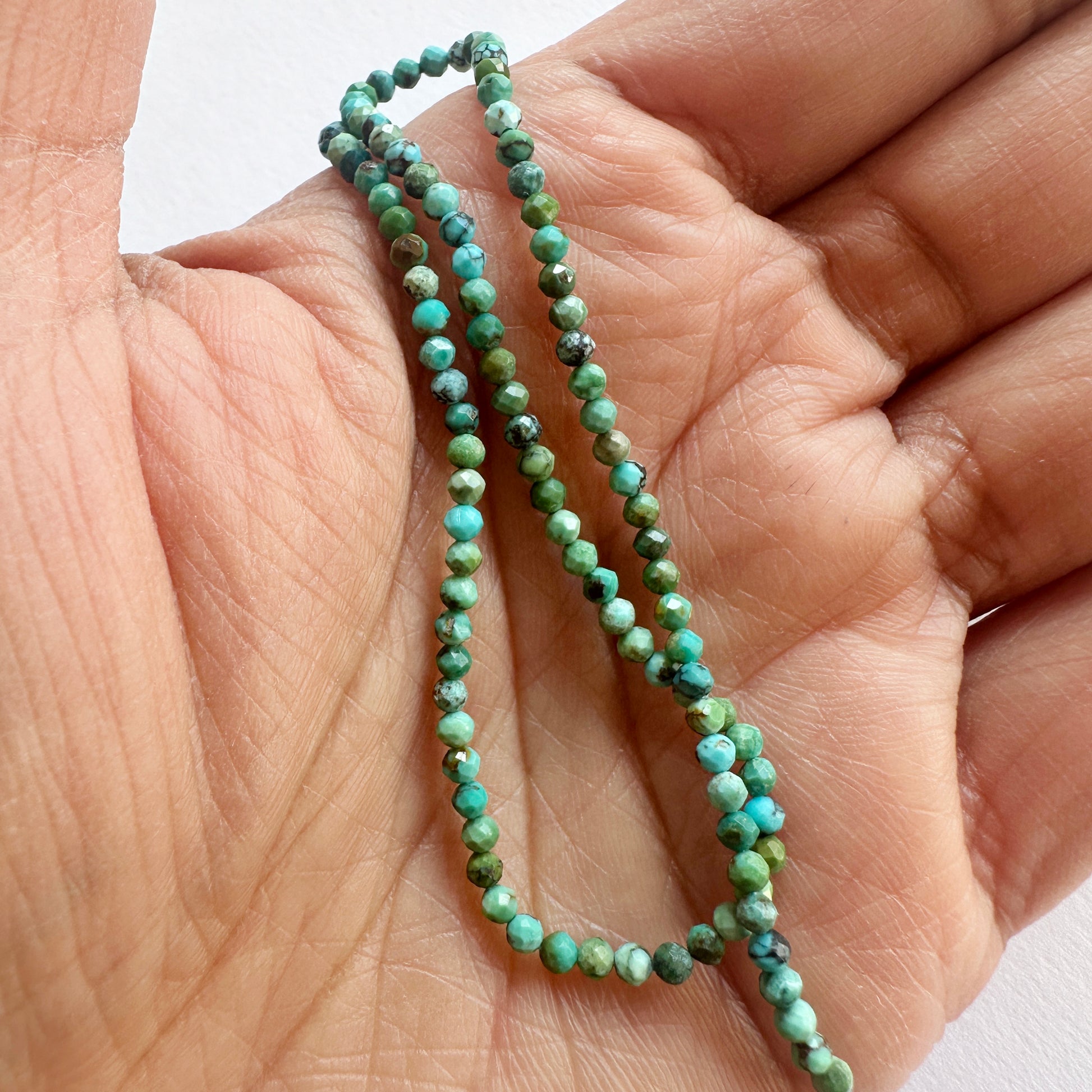 A person holds delicate strands of Chrysocolla beads, showcasing their smooth design.