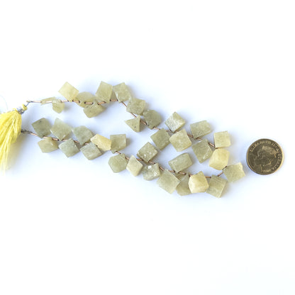 A coin is placed near delicate pieces of Chrysoberyl Cat's Eye drilled rough beads for scale.