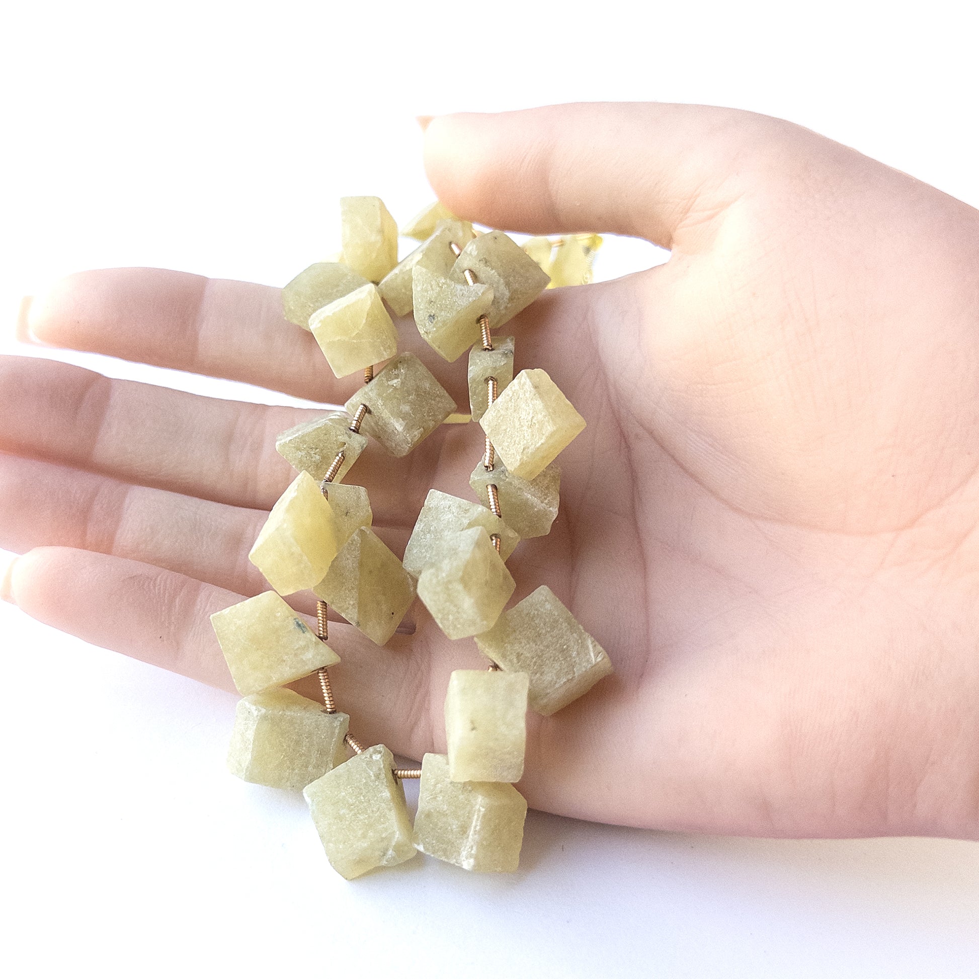 A person holds delicate strands of Chrysoberyl Cat's Eye drilled rough beads, showcasing their rough design.
