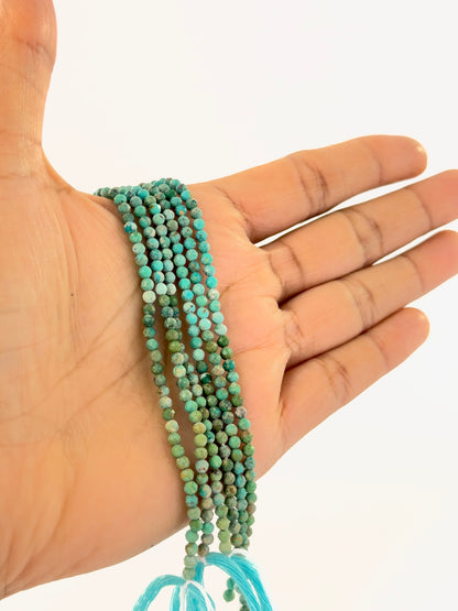 A person holds delicate strands of Chrysocolla beads, showcasing their faceted rondelle design.