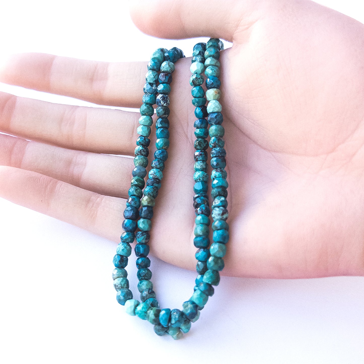 A person holds delicate strands of Chrysocolla beads, showcasing their faceted rondelle design.