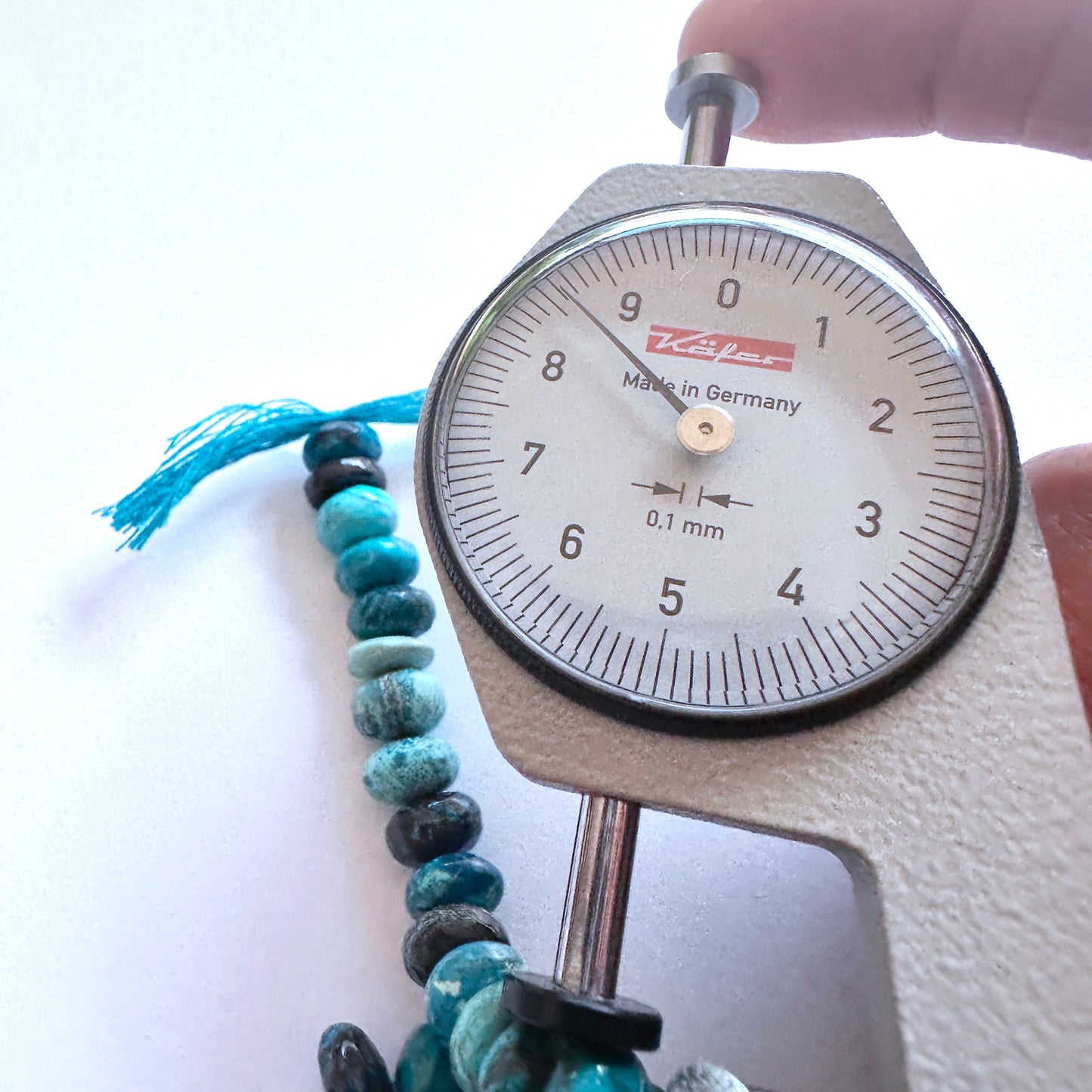 A dial gauge measures the Chrysocolla smooth rondelle gemstone.