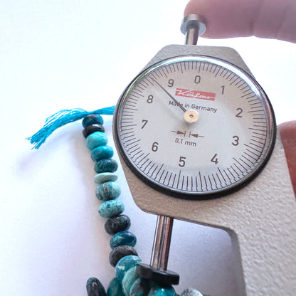 A dial gauge measures the Chrysocolla smooth rondelle gemstone.