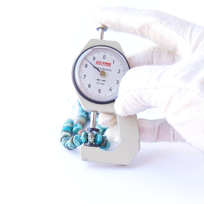 A dial gauge measures the Chrysocolla smooth rondelle 8mm gemstone.