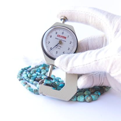 A dial gauge measures the Chrysocolla smooth tumble 5.5–8.5mm gemstone.  