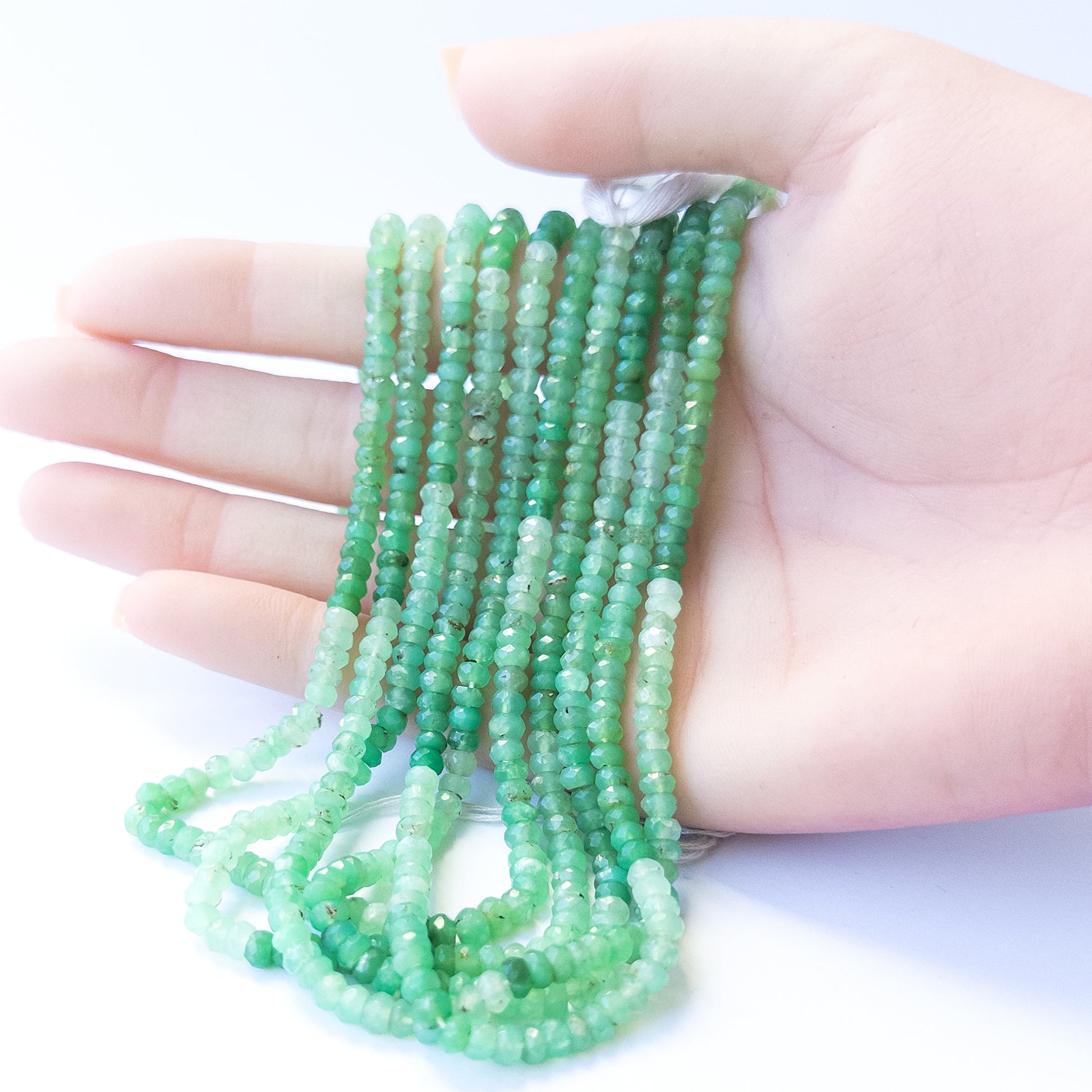 A person holds delicate strands of Chrysoprase beads, showcasing their faceted rondelle design.