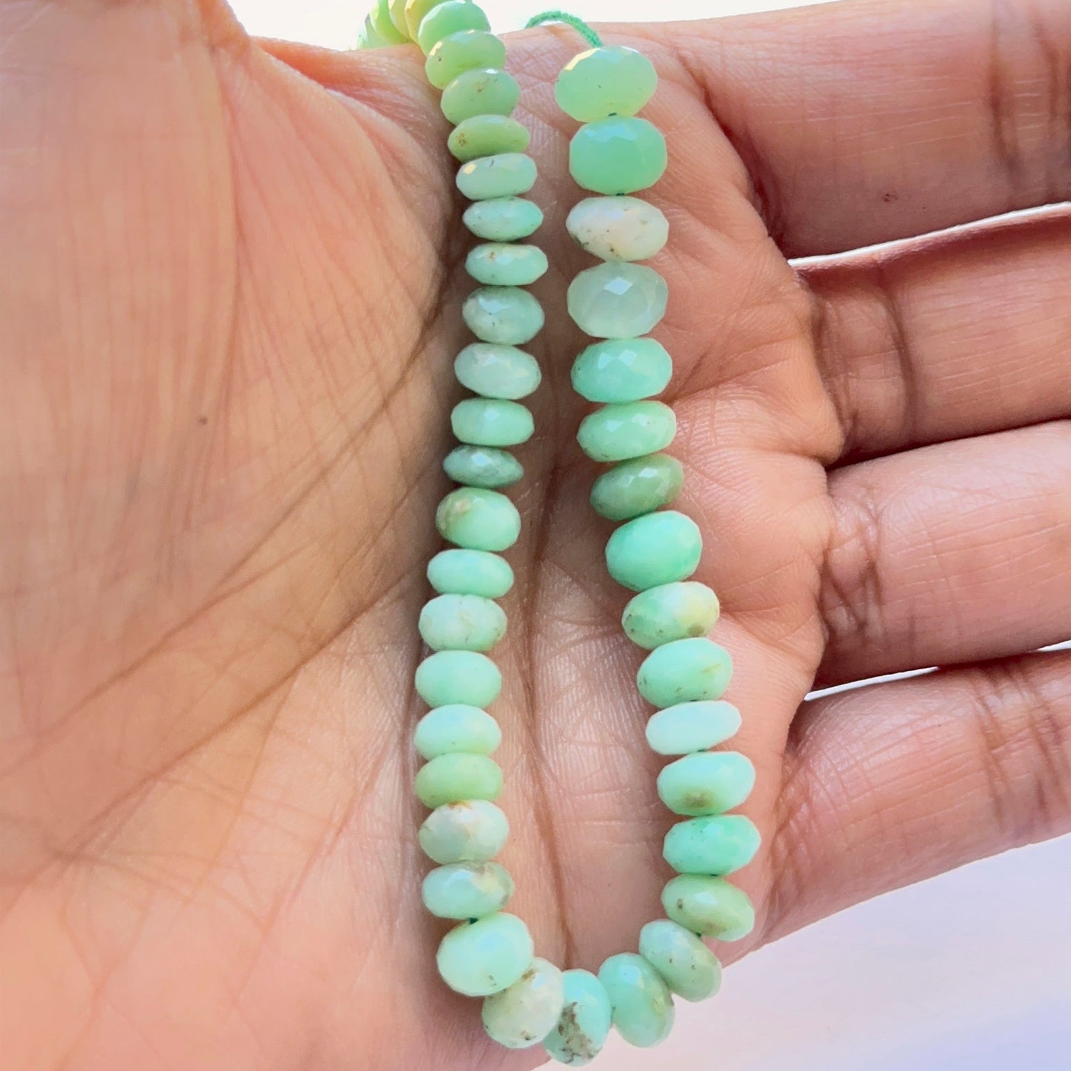 A person holds delicate strands of Chrysoprase beads, showcasing their smooth design.