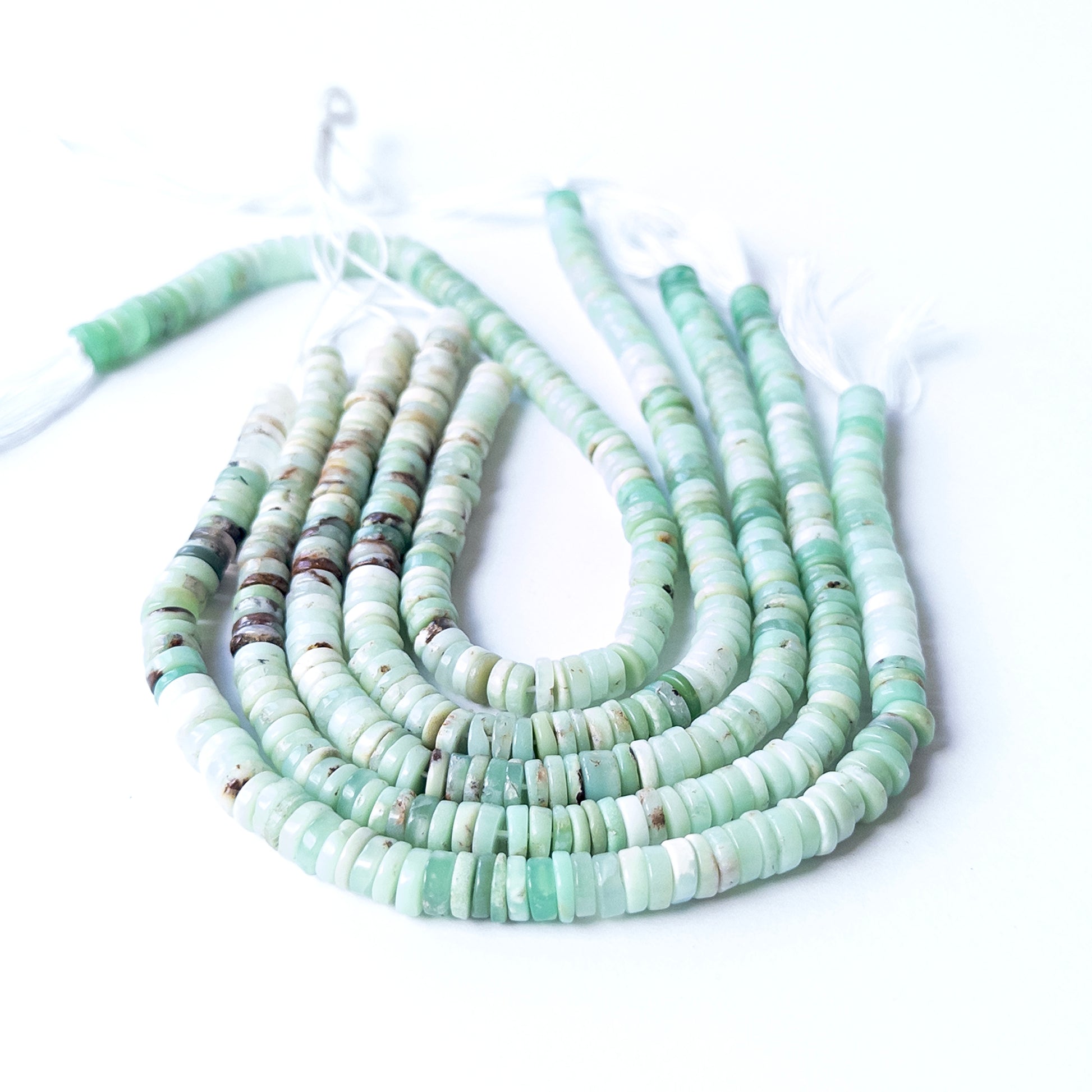 Chrysoprase smooth wheel heishi gemstone beads arranged in a strand showing bright green colour and polished finish.