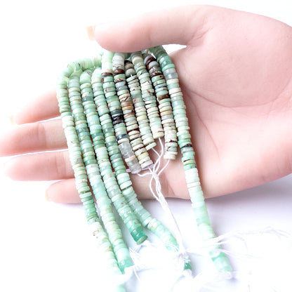 A person holds delicate strands of Chrysoprase beads, showcasing their smooth wheel heishi design.