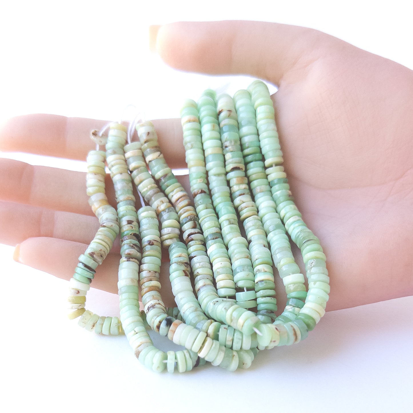 A person holds delicate strands of Chrysoprase smooth wheel beads, showcasing their polished design.