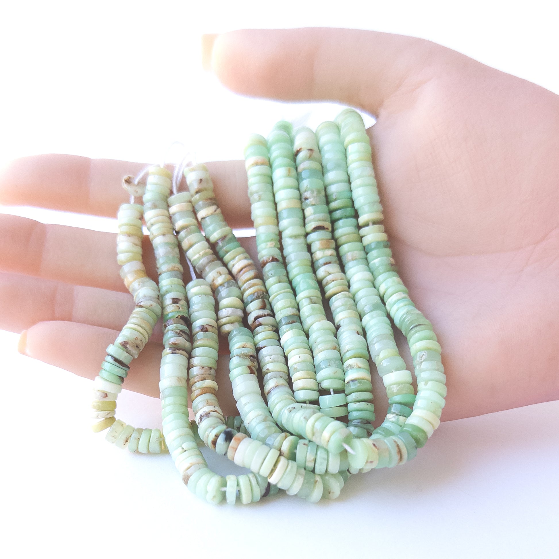 A person holds delicate strands of Chrysoprase smooth wheel beads, showcasing their polished design.